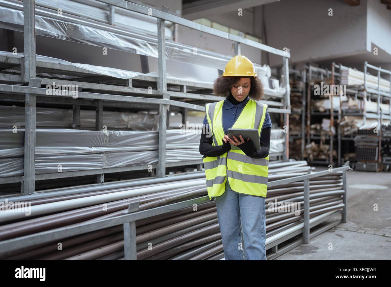 Lavoratrice donna in una fabbrica di prodotti metallici che fa l'inventario delle merci e controlla le scorte in un magazzino aperto utilizzando un tablet digitale. Foto Stock