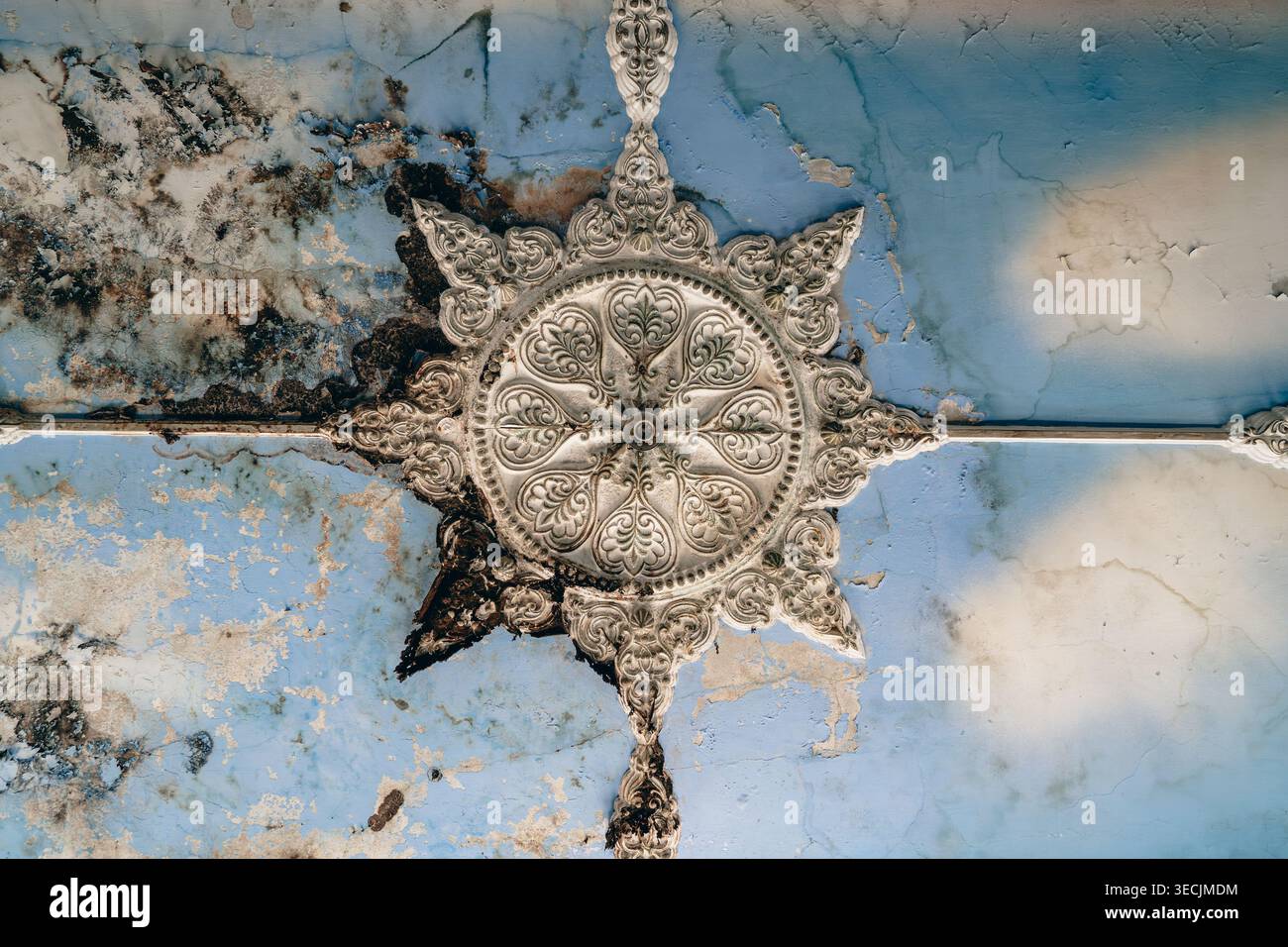 Medaglione del soffitto decorato danneggiato su intonaco blu incrinato, decadimento della muffa, dettagli architettonici vintage, sfondo texture di restauro. Foto Stock
