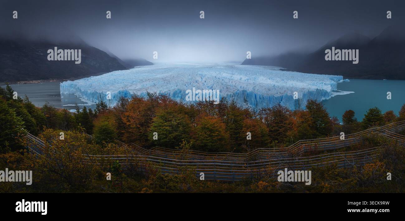 Ampia vista panoramica del ghiacciaio Perito Moreno in Patagonia, Argentina, con scogliere di ghiaccio blu che incontrano un lago turchese, montagne nebbiose e fores autunnali Foto Stock