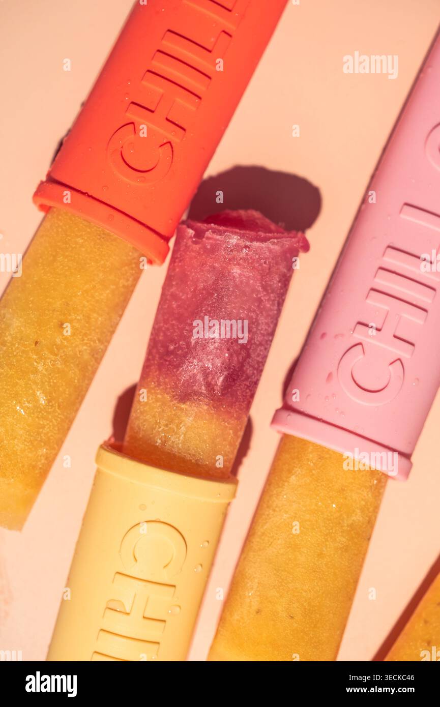 Primo piano di ghiaccioli di frutta fatti in casa in stampi colorati riutilizzabili, che mostrano strati vibranti e consistenza gelata su uno sfondo pastello, perfetto per la somma Foto Stock