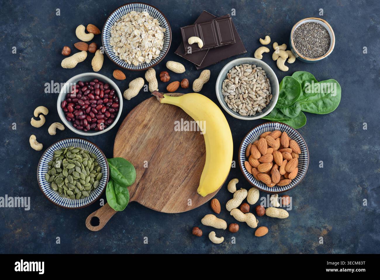 Vista dall'alto di cibi ricchi di magnesio disposti su sfondo scuro, tra cui avena, cioccolato, semi di chia, girasole e semi di zucca, noci, banana, spinning Foto Stock