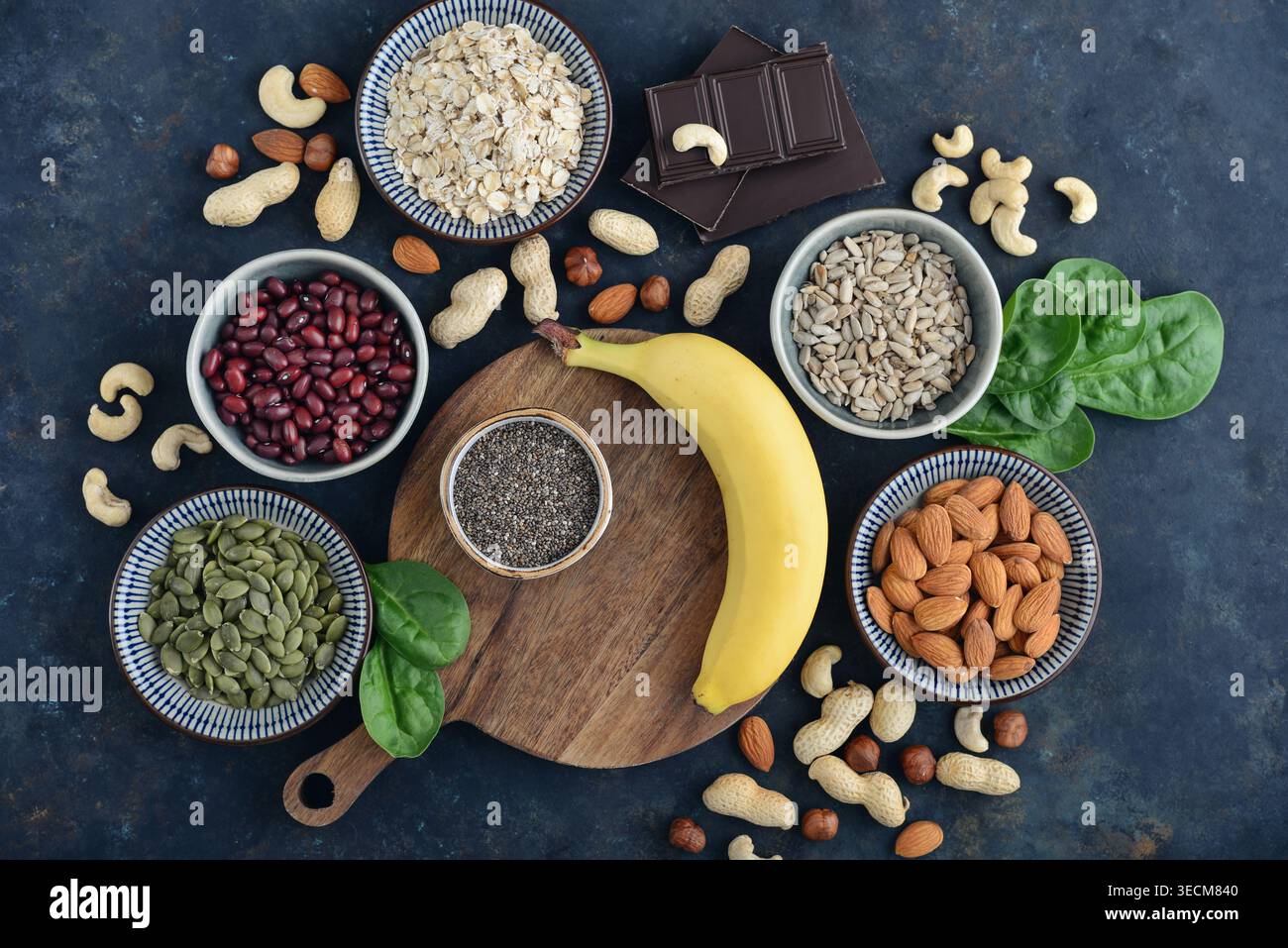Vista dall'alto di cibi ricchi di magnesio disposti su sfondo scuro, tra cui avena, cioccolato, semi di chia, girasole e semi di zucca, noci, banana, spinning Foto Stock