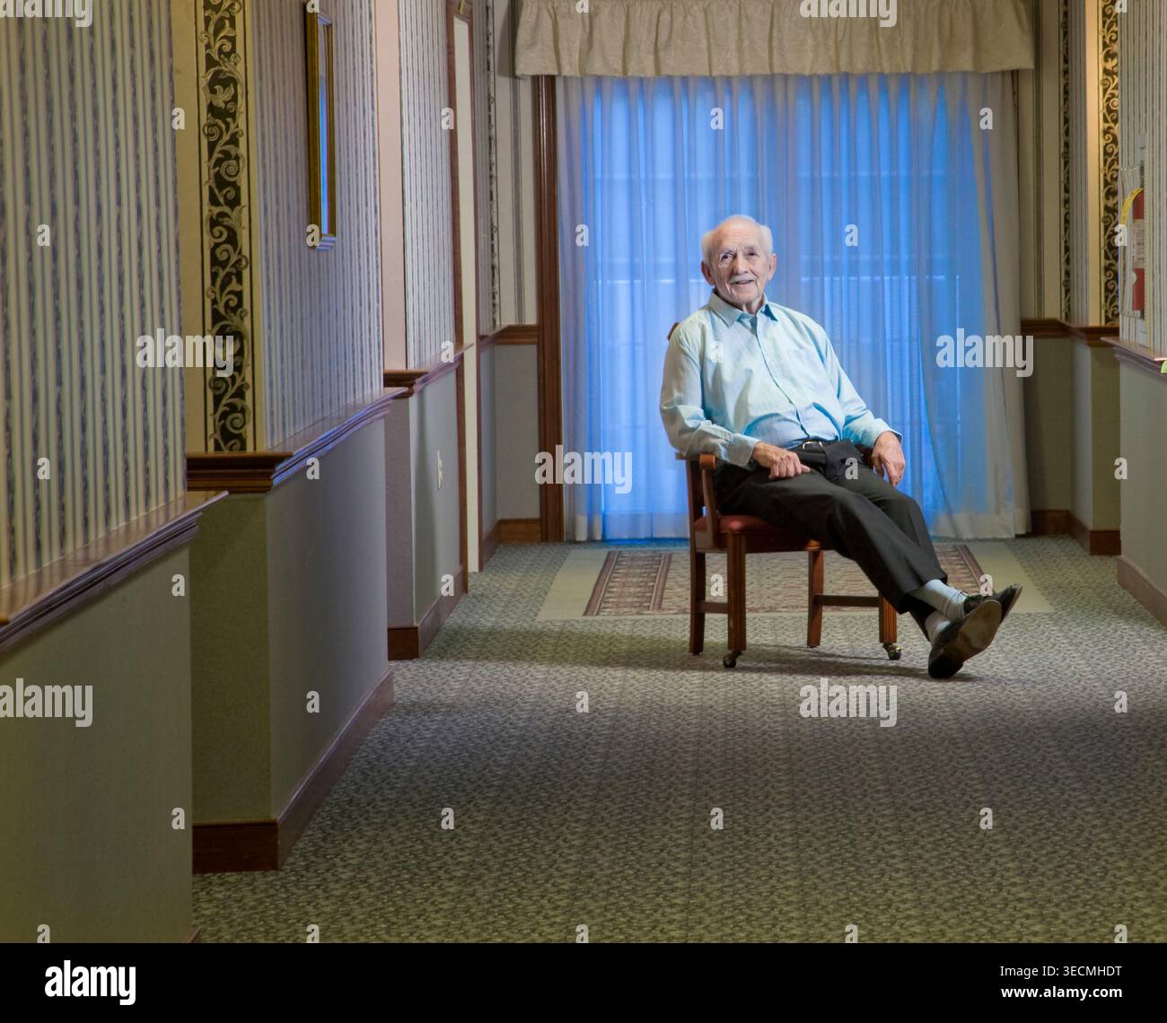 Un uomo anziano seduto sulla sedia nel corridoio sorridente, Philadelphia USA Foto Stock