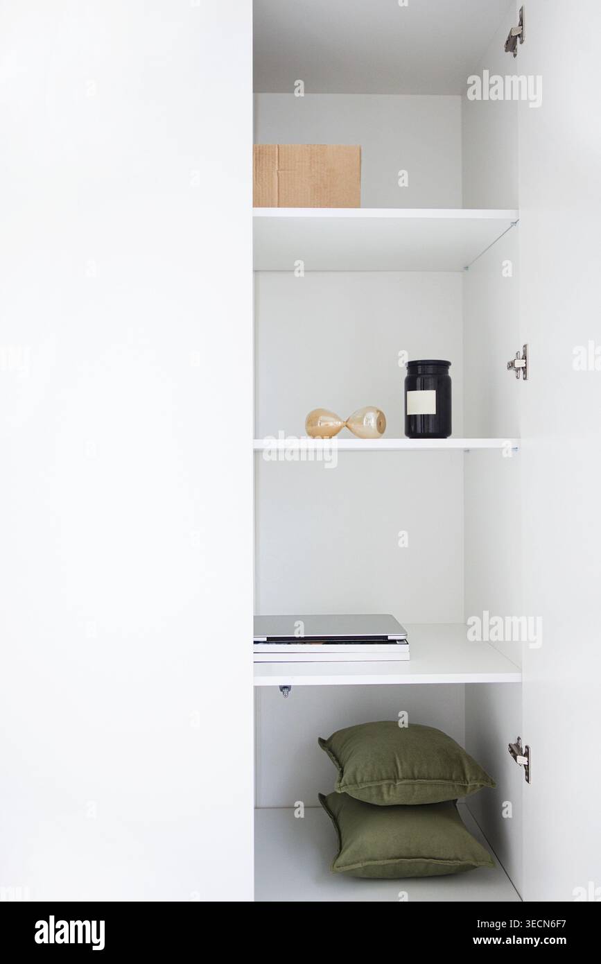Interno di un armadietto bianco minimalista con ripiani con vaso nero, clessidra, scatola decorativa e cuscini verdi per un aspetto ordinato Foto Stock