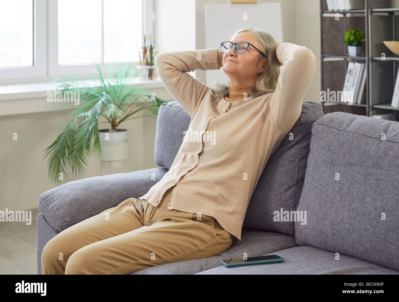 Donna anziana felice che si rilassa sul divano a casa Foto Stock