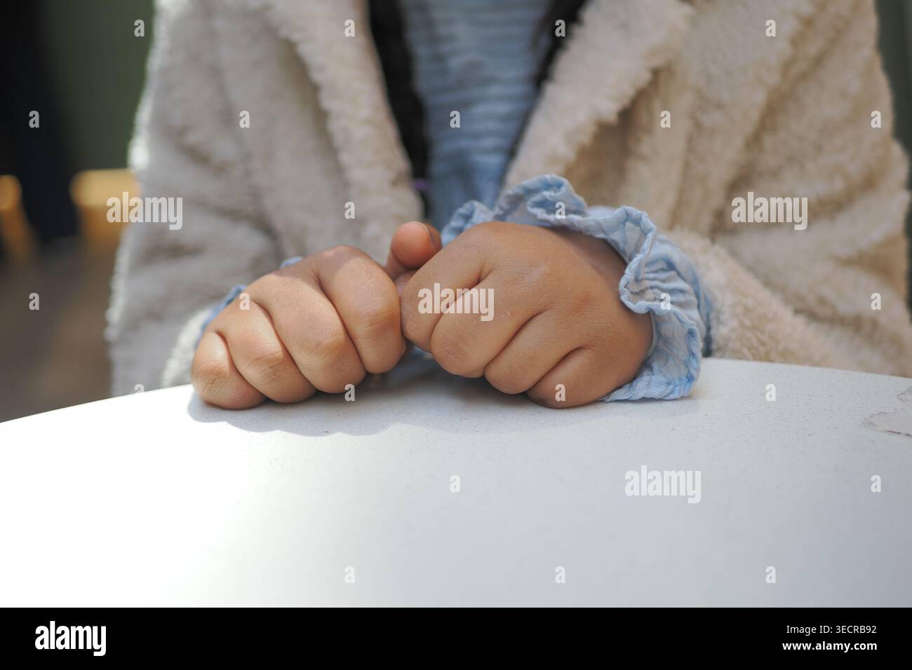 Il bambino siede al tavolo con le mani agganciate in posizione di attesa Foto Stock