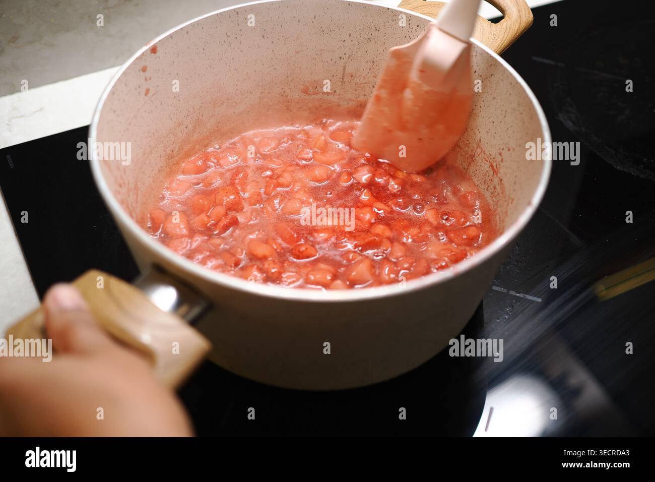 Cuocere il composto di frutta in una pentola su un piano cottura per preparare una marmellata di mirtilli Foto Stock