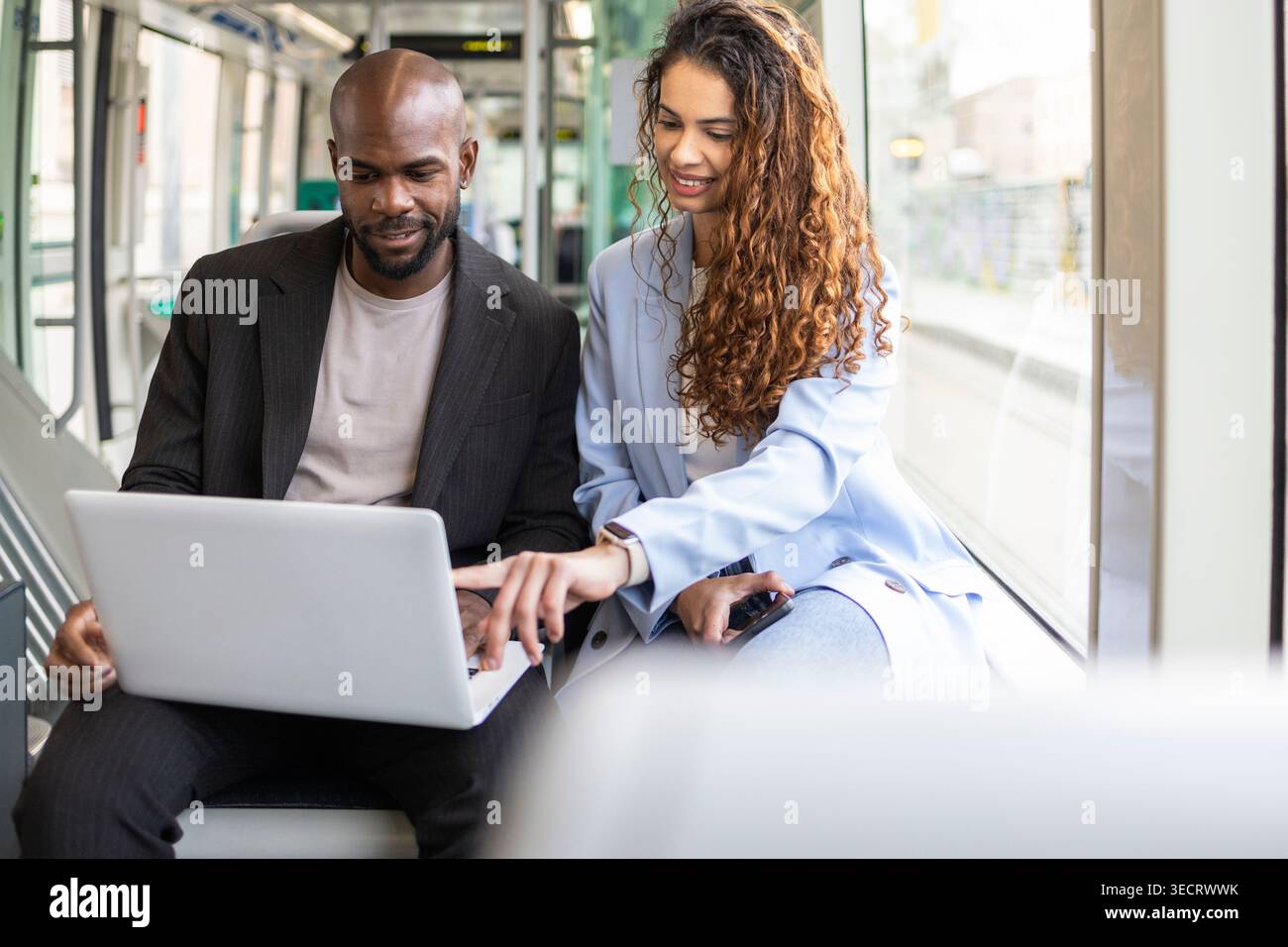 Una coppia di lavoro in viaggio di lavoro utilizza un computer portatile e uno smartphone su un treno moderno, rivedendo piani e documenti insieme durante gli spostamenti per un team mobile Foto Stock