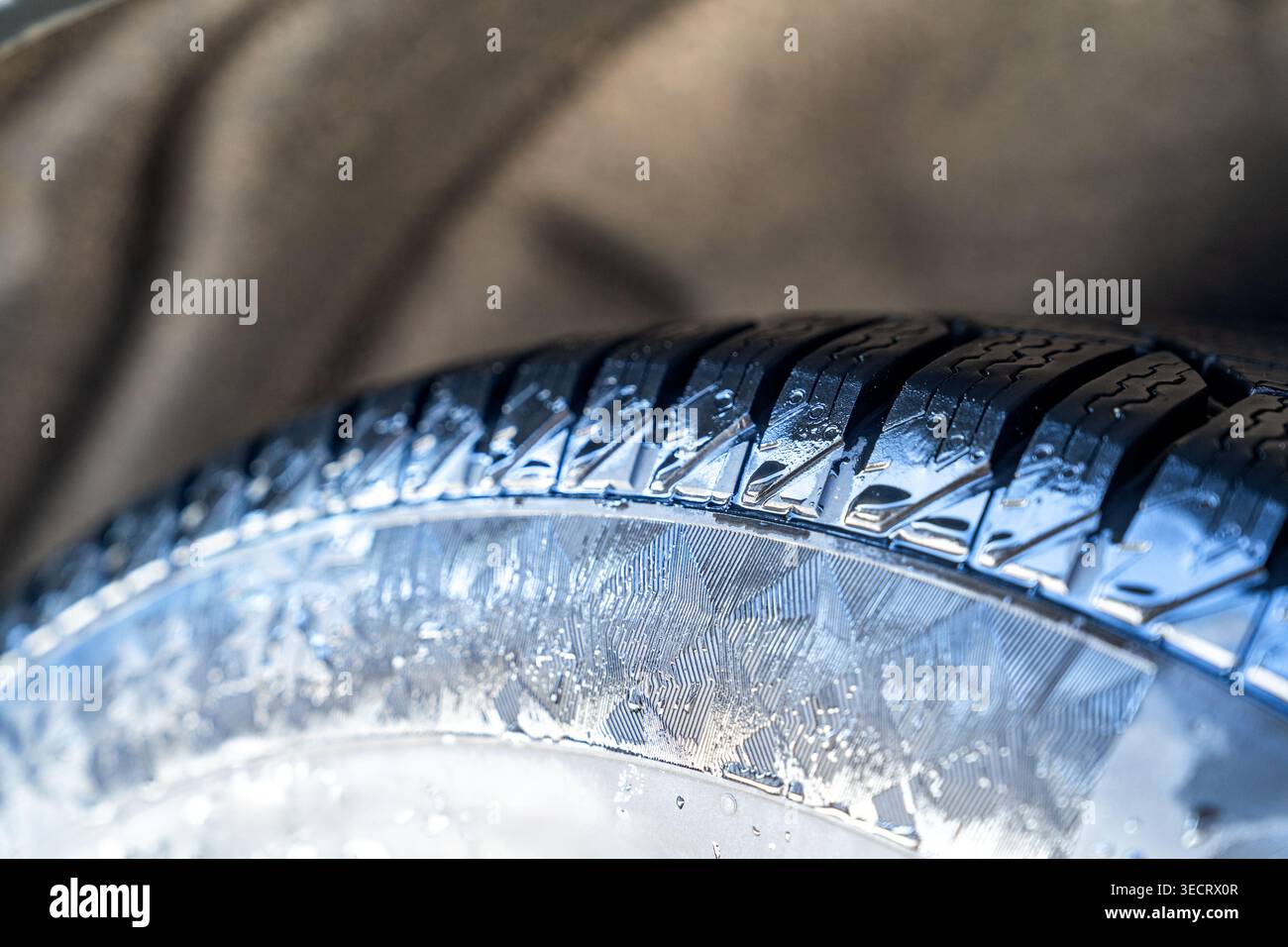 Primo piano di una ruota bagnata che mostra un battistrada dettagliato e un cerchio in lega lucida con gocce d'acqua, suggerendo una guida piovosa, sicurezza, trazione, a. Foto Stock