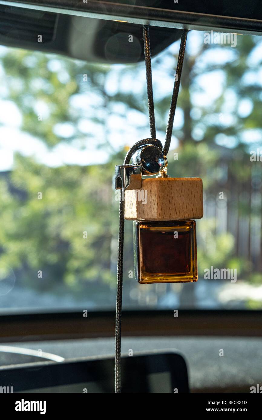 Primo piano di una bottiglia di deodorante per auto appesa con tappo e cordoncino in legno, riempita di olio profumato ambrato, illuminata dalla luce del sole contro un outdo morbido e sfocato Foto Stock
