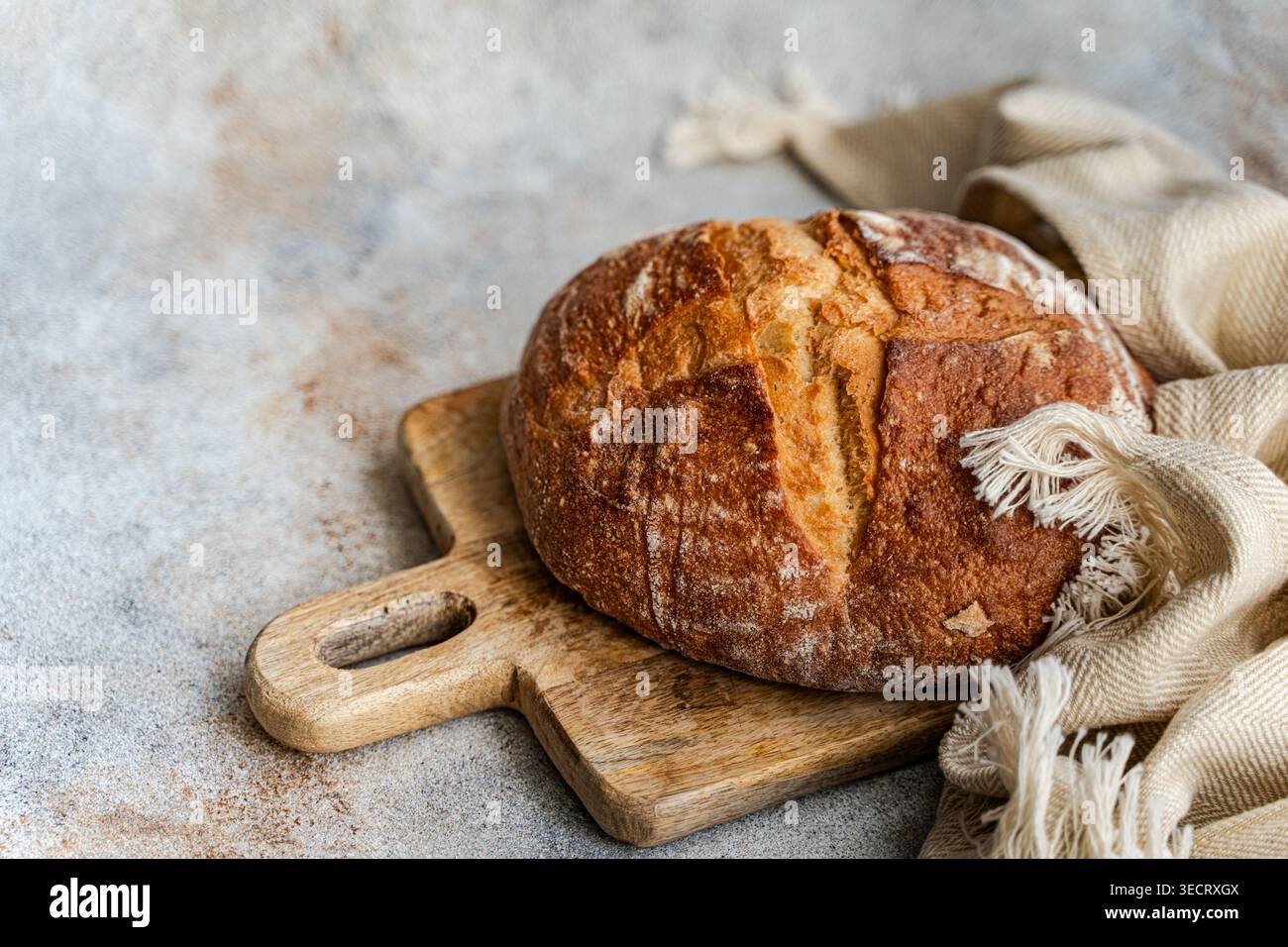 Pane rustico a lievito naturale con crosta dorata su un tagliere di legno accanto a un tovagliolo di lino, su uno sfondo di pietra chiara con spazio per copiare il testo. Foto Stock