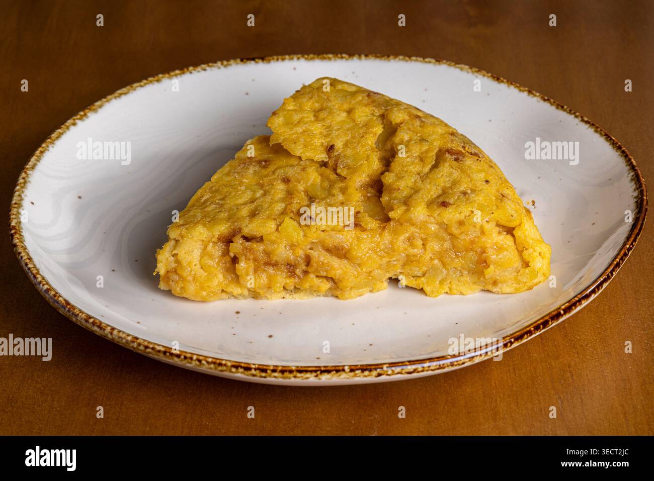 Primo piano di una fetta di tortilla spagnola servita su un piatto di ceramica rustica, semplice cibo fatto in casa per la colazione sparato in una luce calda, perfetto per la mattina Foto Stock