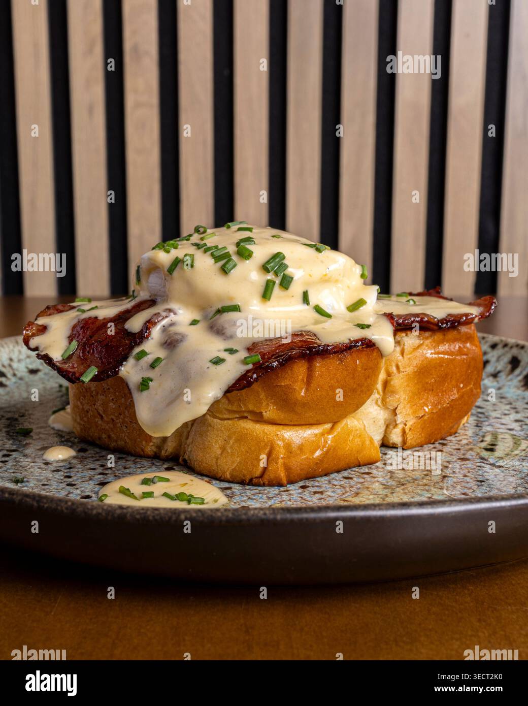 Primo piano delle uova della colazione benedict servite su un pane tostato denso con pancetta croccante, uova in camicia e salsa cremosa, condita con erba cipollina, su un rusti Foto Stock