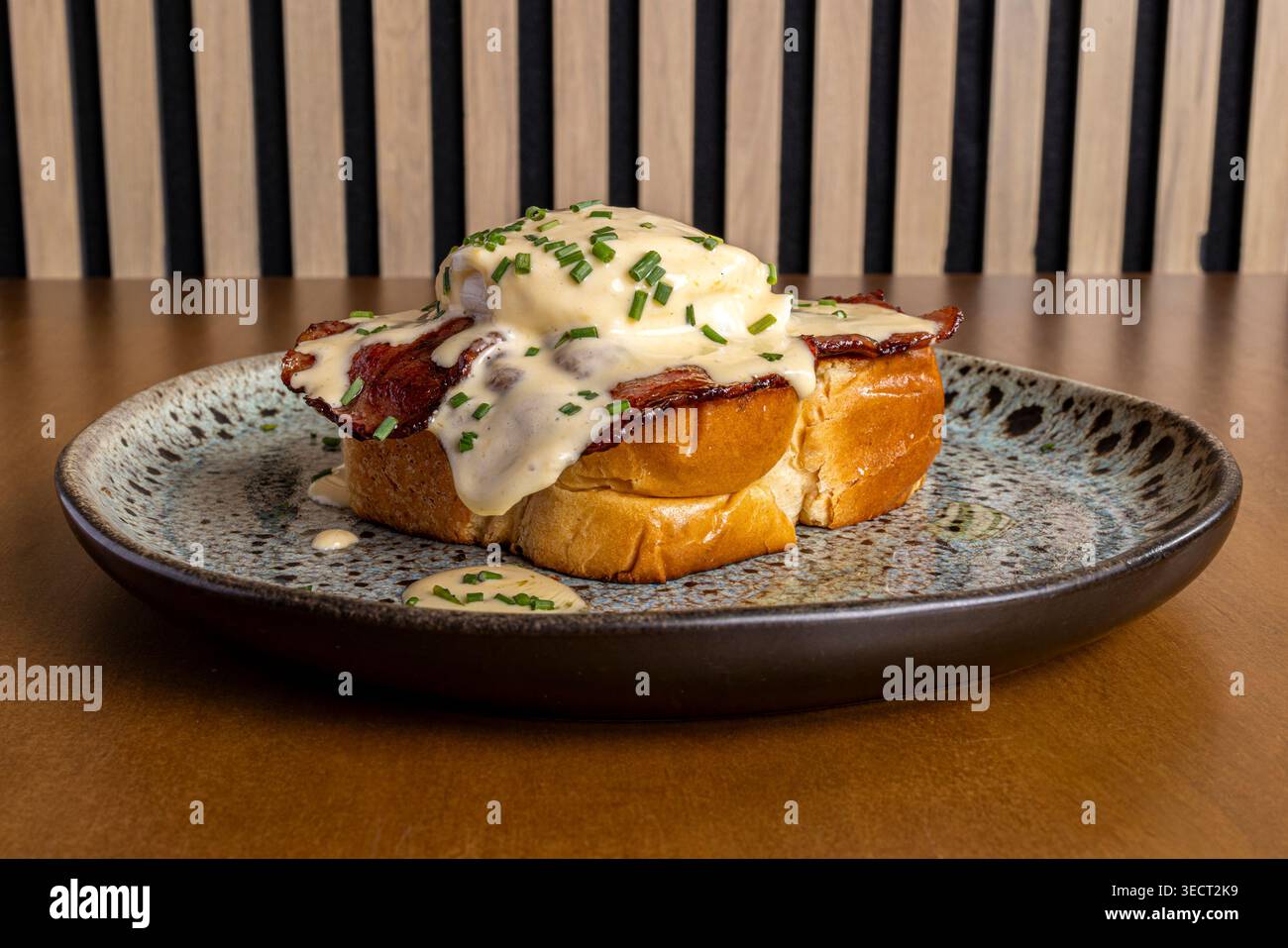 Primo piano del toast della colazione ricoperto di pancetta croccante, uovo in camicia e salsa cremosa, decorata con erba cipollina, servita su un piatto di ceramica Foto Stock