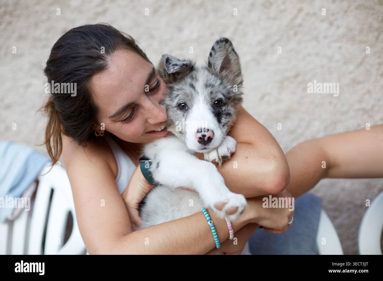 Primo piano di una donna sorridente che abbraccia un morbido cucciolo di collie con pelliccia blu merle. Simpatici cani e cuccioli che si uniscono, all'aperto, in morbido colore naturale Foto Stock