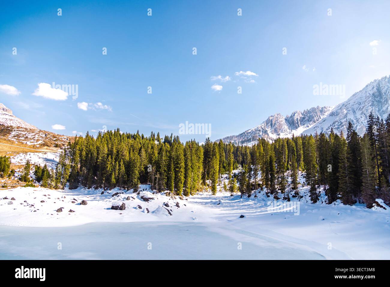 Lago di Carezza ghiacciato in inverno, circondato da neve, foresta sempreverde e cime dolomitiche sotto il cielo azzurro, alto Adige, provincia di Bolzano, Italia. Foto Stock