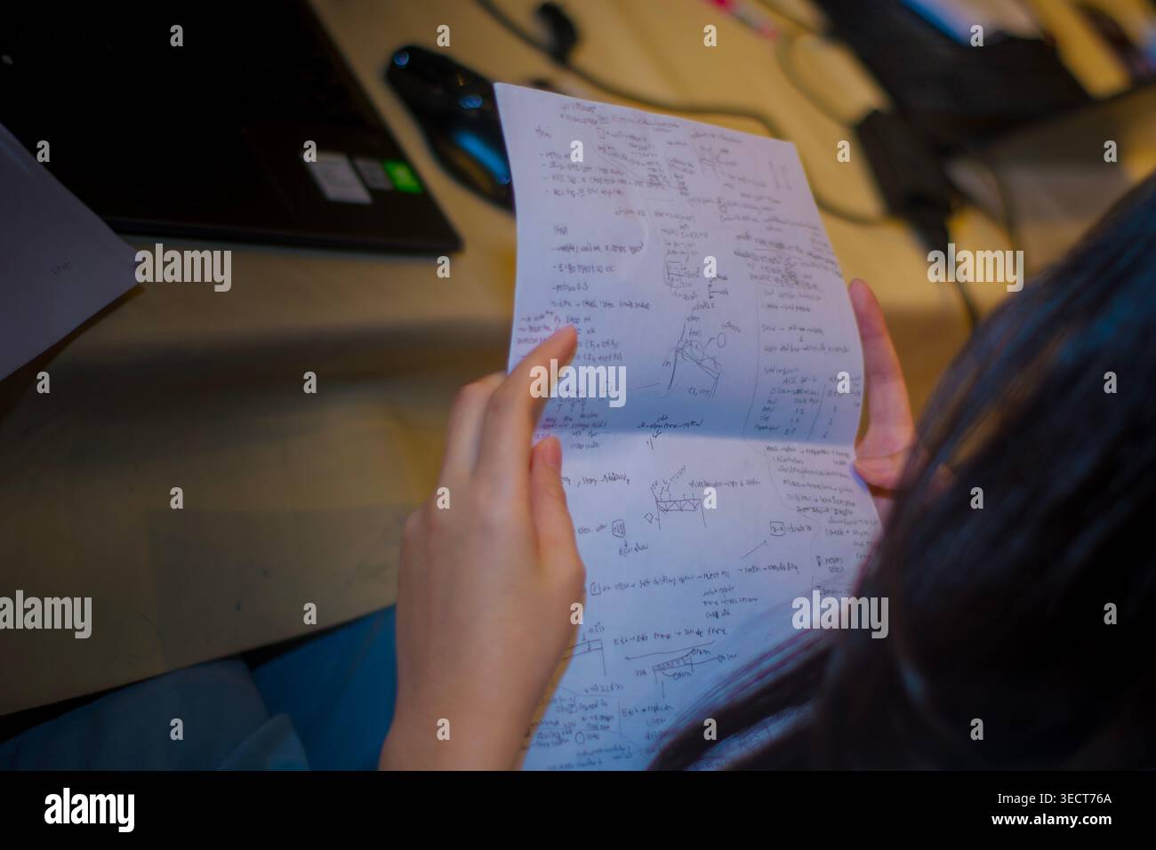 Un ingegnere che esamina un documento manoscritto con diagrammi a corpo libero e equazioni di forza accanto a un laptop durante un corso di progettazione strutturale a Bangkok. Foto Stock