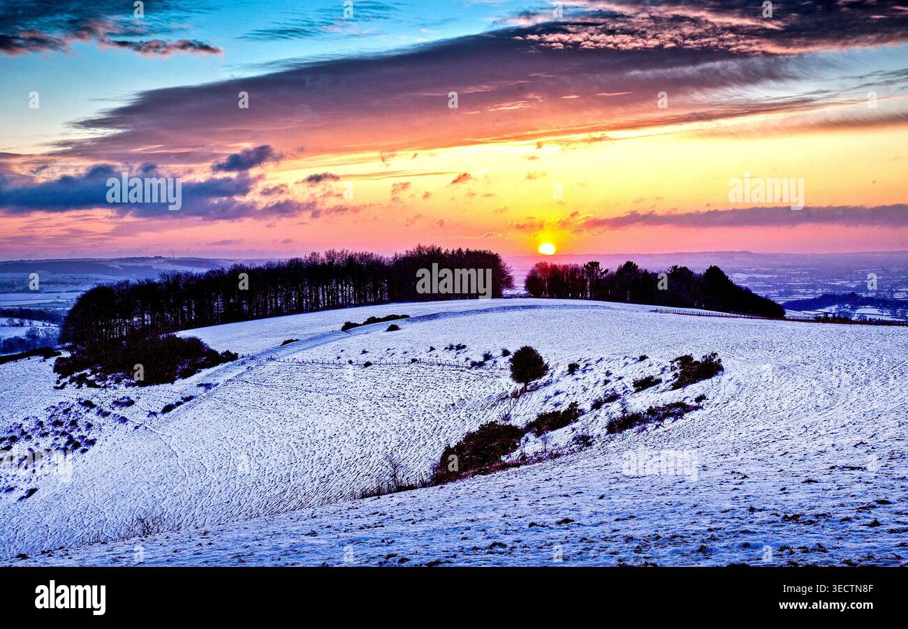 Tramonto invernale su Fontmell Down, il Dorset UK dipinge le colline innevate di rosa e oro, catturando la tranquilla bellezza di una serata gelida al tramonto in inverno. Foto Stock