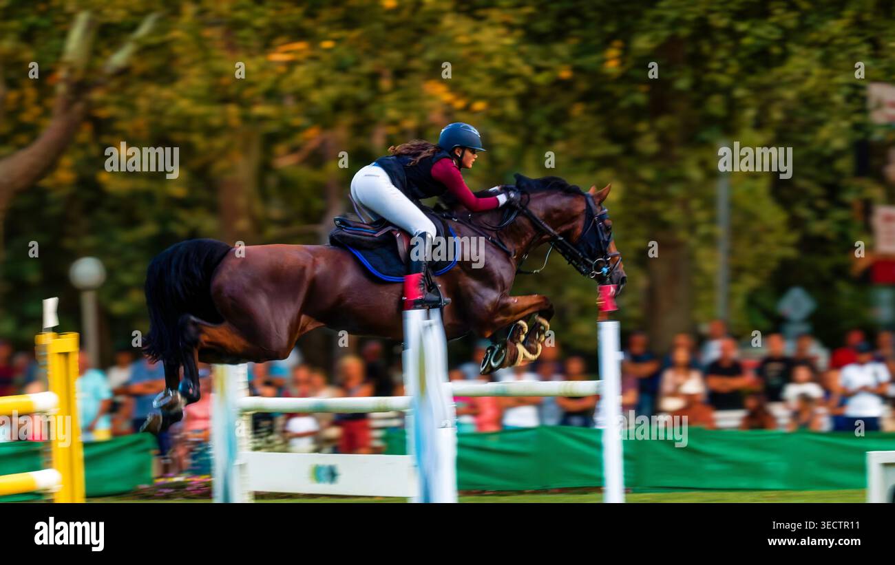 Action Shot dinamico di cavalli e cavalieri durante la gara di salto con lo spettacolo Foto Stock