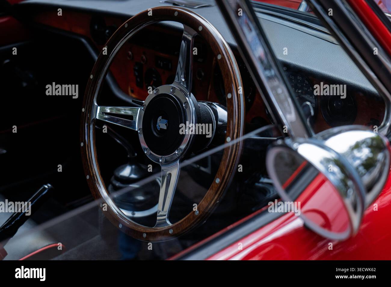 Attraverso la vista del parabrezza della classica auto sportiva Triumph GT6 rossa con volante in legno e specchio cromato Foto Stock