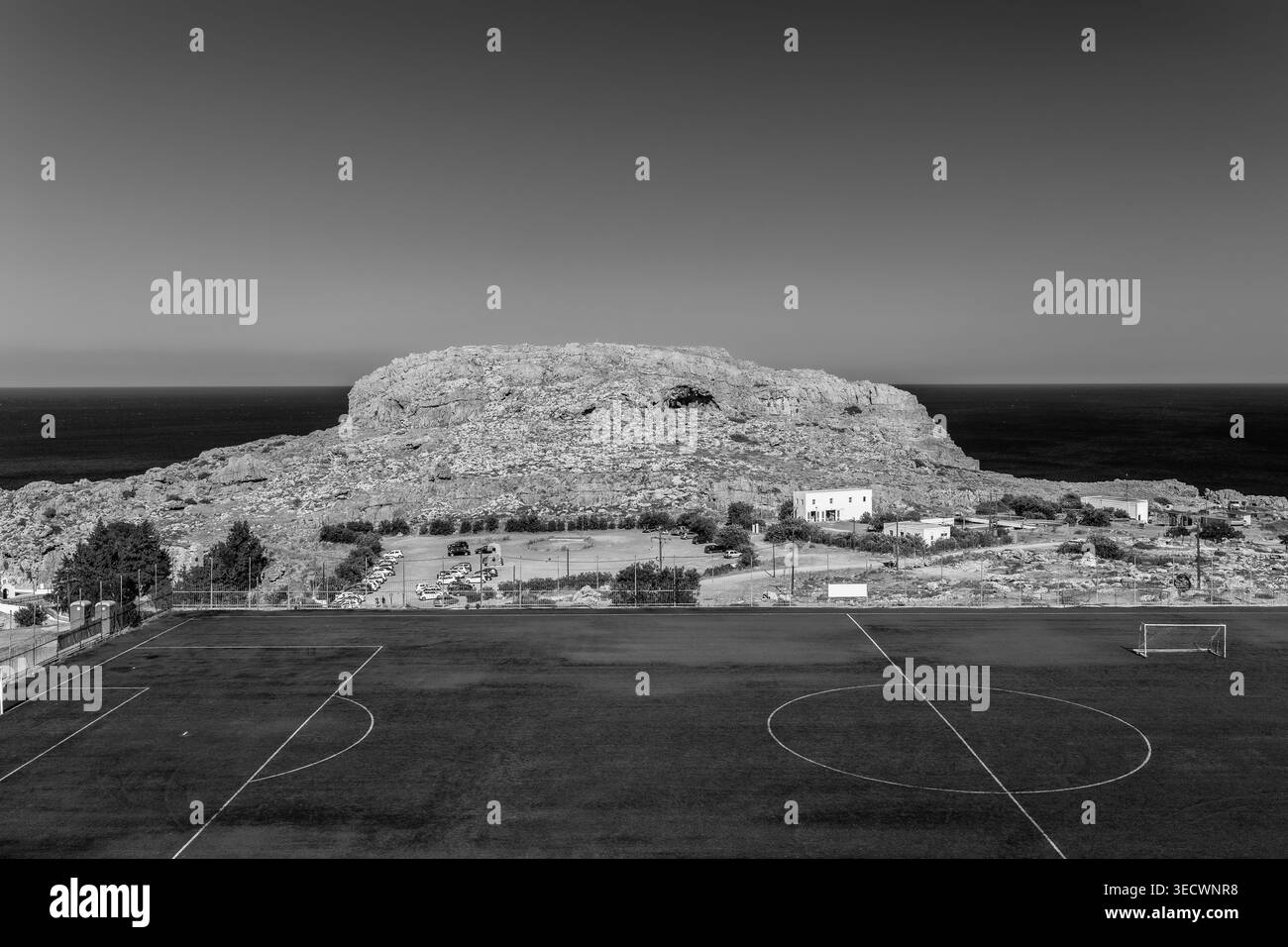 Lindos, lo stadio municipale di calcio vuoto della Grecia, con un grande campo da calcio artificiale circondato da tradizionali edifici bianchi e Foto Stock