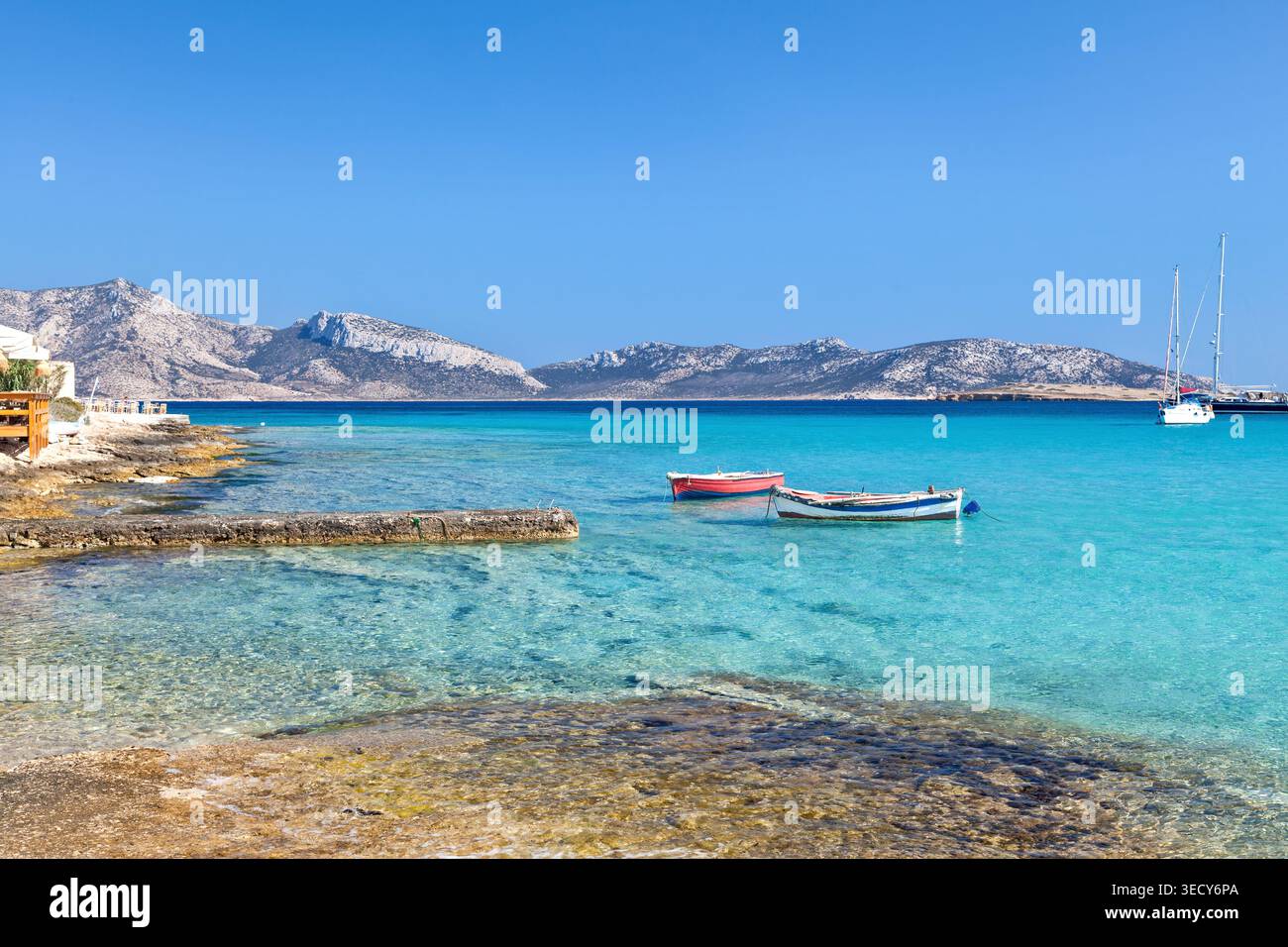 Baia turchese con piccole barche, costa rocciosa e aspre colline delle cicladi nell'isola di Koufonisi, Grecia, Europa, sotto un cielo azzurro. Foto Stock