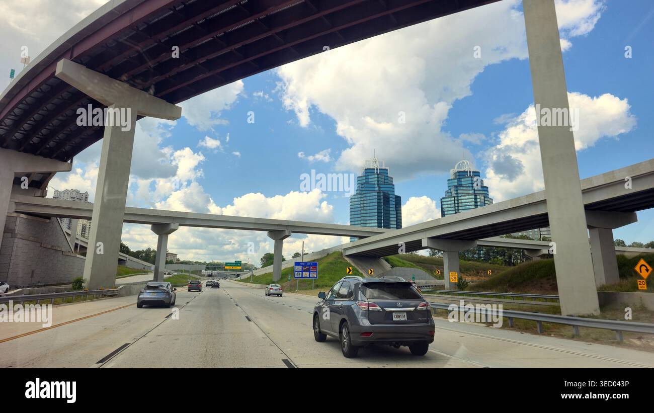 Auto che guidano su un incrocio autostradale a più livelli con superpassaggi e moderne torri di uffici sullo sfondo ad Atlanta, Georgia, Stati Uniti - Immagine stock catturata con smartphone