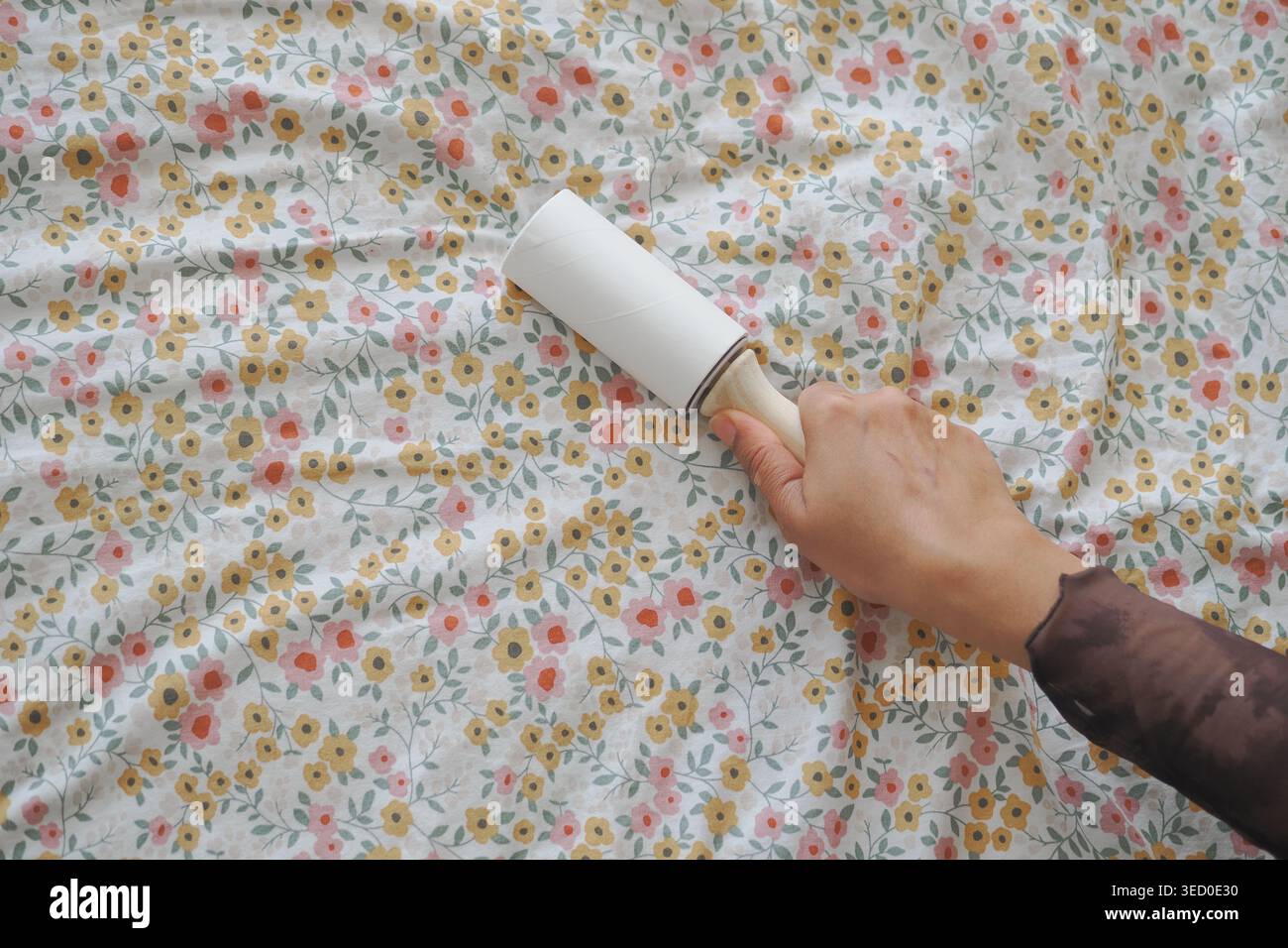 Pulizia di un tessuto con un rullo di lanugine su una stampa floreale Foto Stock