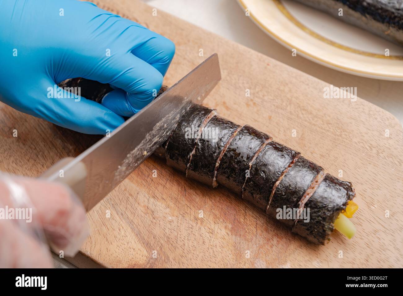 Primo piano di mani che affettano kimbap di riso alle alghe coreane su una tavola di legno Foto Stock
