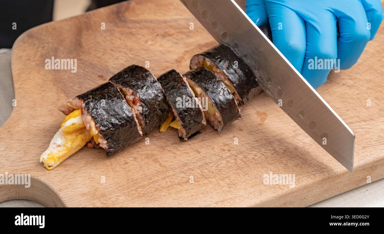Primo piano di mani che affettano kimbap di riso alle alghe coreane su una tavola di legno Foto Stock