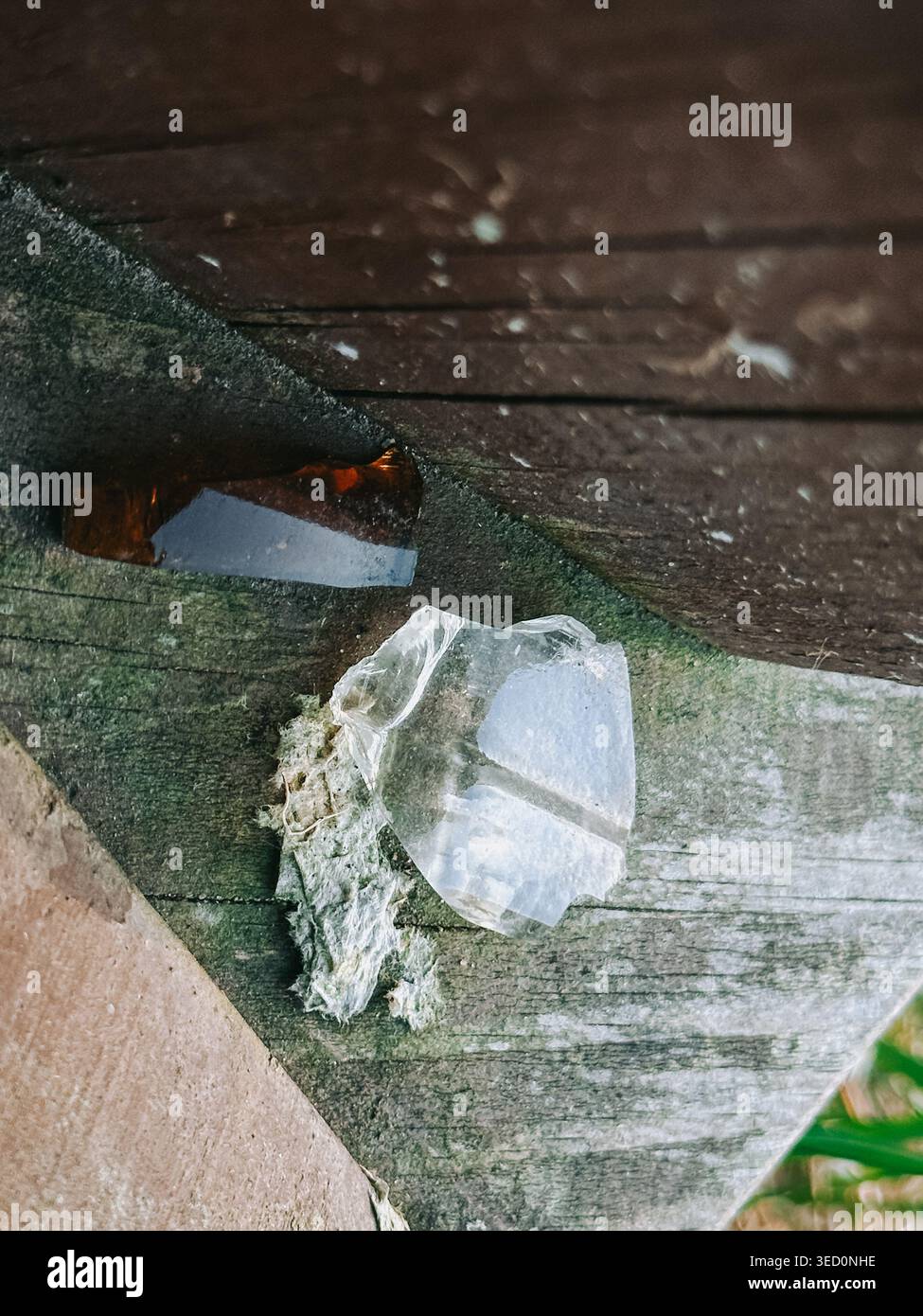Primo piano di frammenti di vetro taglienti e rotti poggiati su tavole di legno invecchiate. Scena ruvida e ruvida che trasporta pericoli, danni e negligenza, ideale per la sicurezza, Foto Stock