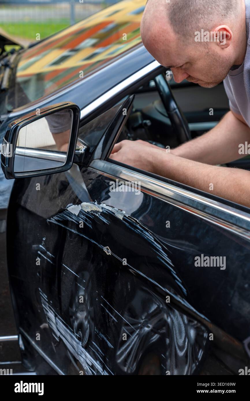 Meccanico professionista che disinnesta meticolosamente i componenti interni delle portiere all'interno del veicolo. Esperto esperto di auto-body che accede pazientemente ai cablaggi e. Foto Stock