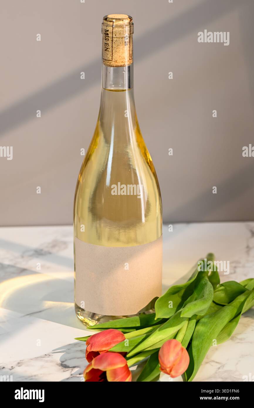 Una bottiglia di vino bianco si stende accanto ai tulipani su marmo. Foto Stock