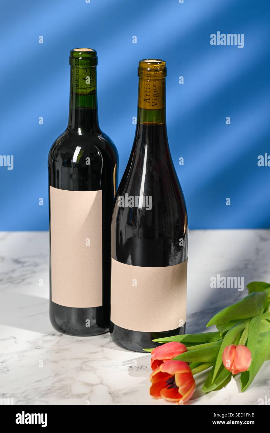 Due bottiglie di vino con etichette semplici accanto ai tulipani su un tavolo Foto Stock