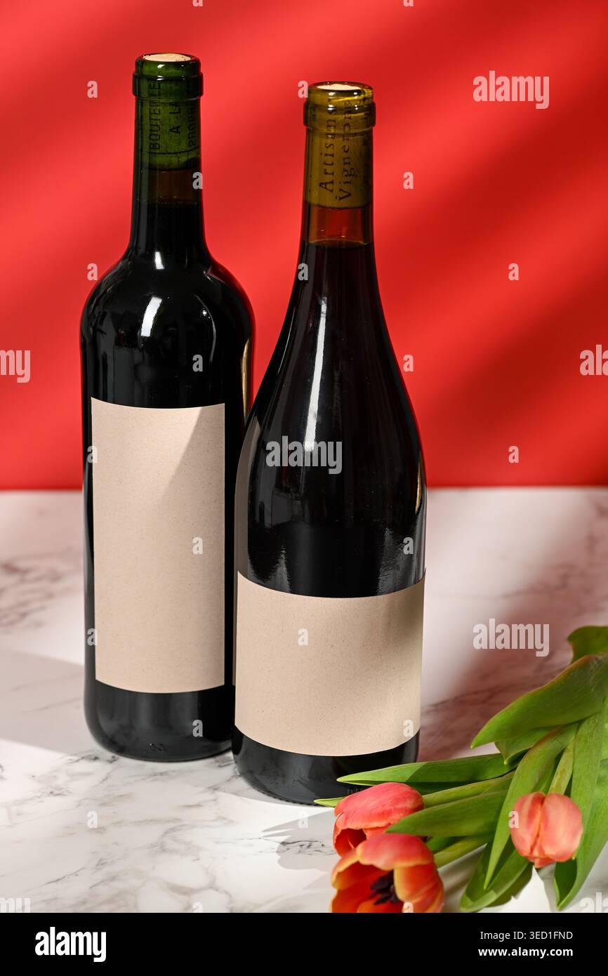 Due bottiglie di vino si stendono su una superficie di marmo con tulipani. Foto Stock