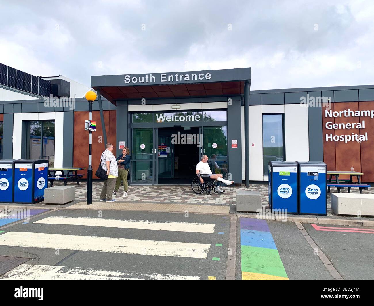 Vista esterna del Northampton General Hospital UK con visitatori e sedie a rotelle accesso visibile ingresso principale nuovo edificio zebra crossing - Immagine stock catturata con smartphone