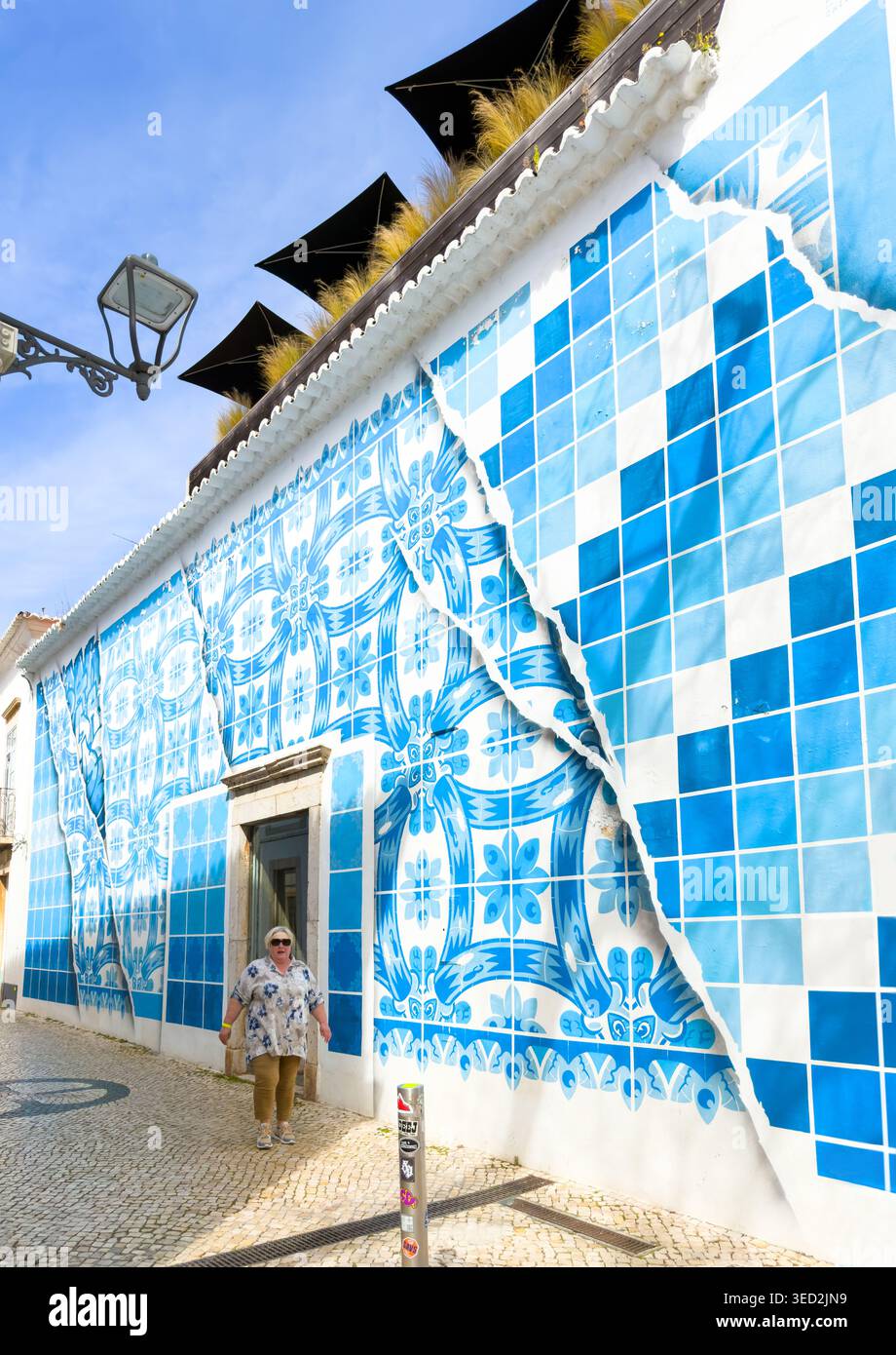 Donna che cammina davanti a una facciata di un edificio caratterizzato da un contemporaneo murale di piastrelle azulejo blu e bianche con un design di carta strappata in una città portoghese Foto Stock