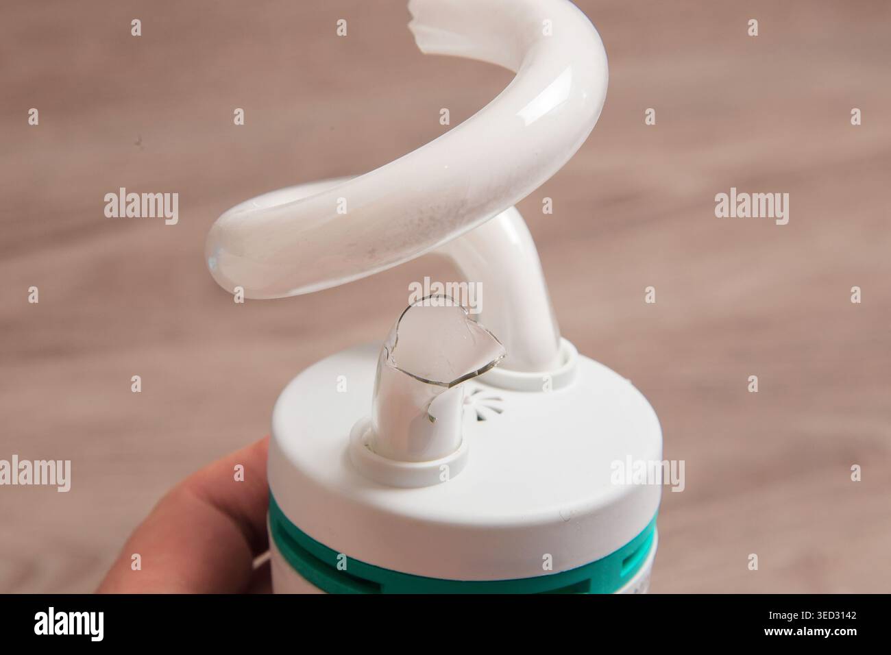 La lampada a spirale bianca ha una base incrinata. Il cappuccio circolare mostra danni evidenti. Un background minimo enfatizza il difetto Foto Stock