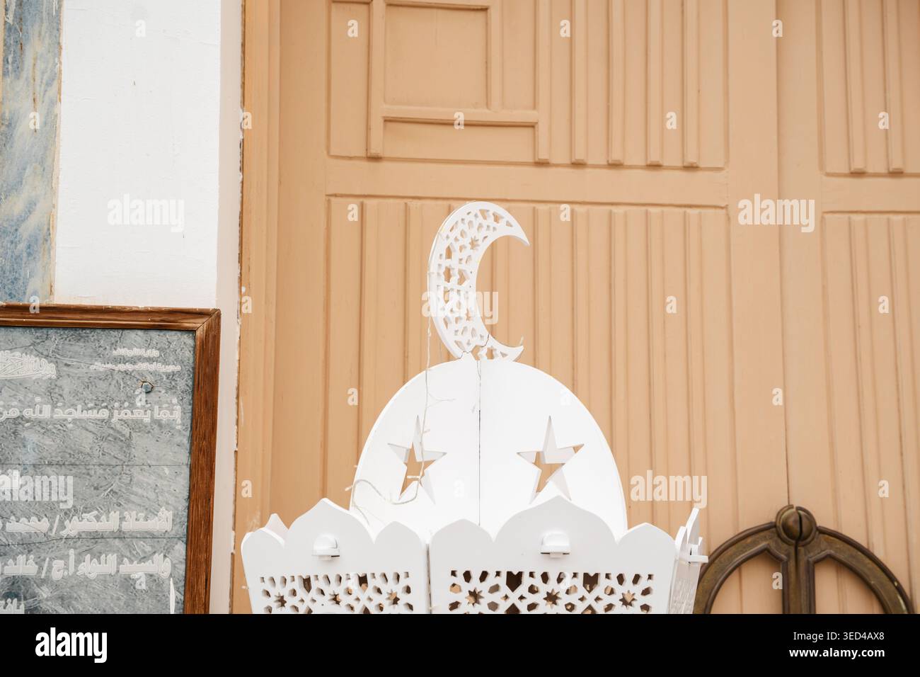 Lanterna decorativa da moschea con mezzaluna e intagli a stella collocata vicino alla porta d'ingresso in legno e placca di iscrizione sulla parete. Elemento di illuminazione islamico est Foto Stock