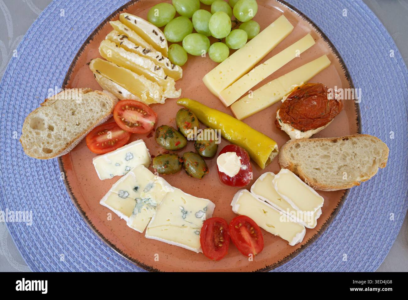 Un appetitoso tagliere di formaggi con formaggio blu, camembert, uva, olive, pomodori, e pane fresco su un piatto di terracotta Foto Stock