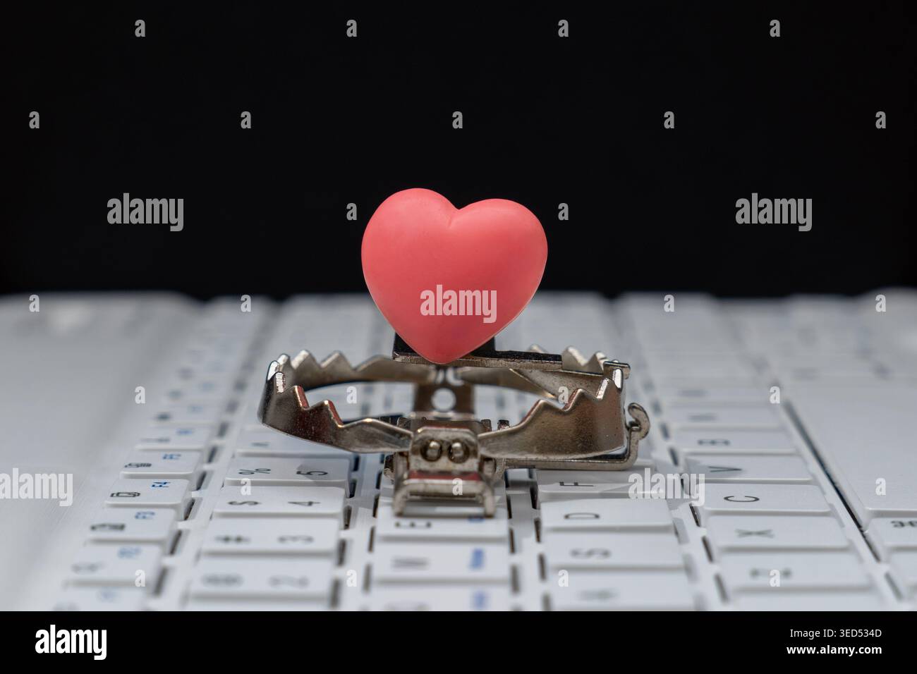Una trappola di metallo impregnata di un cuore rosa su una tastiera bianca per computer. Truffe di incontri online, truffe romantiche, pesca gatto, concetto di truffa amorosa. Foto Stock