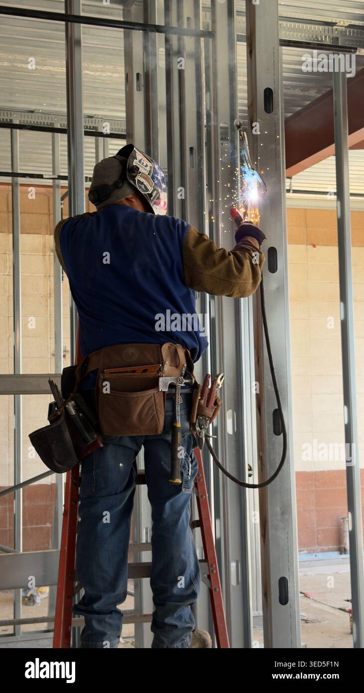 Il lavoratore edile salda prigionieri metallici in interni con scintille e dispositivi di protezione in un cantiere di Los Angeles Foto Stock