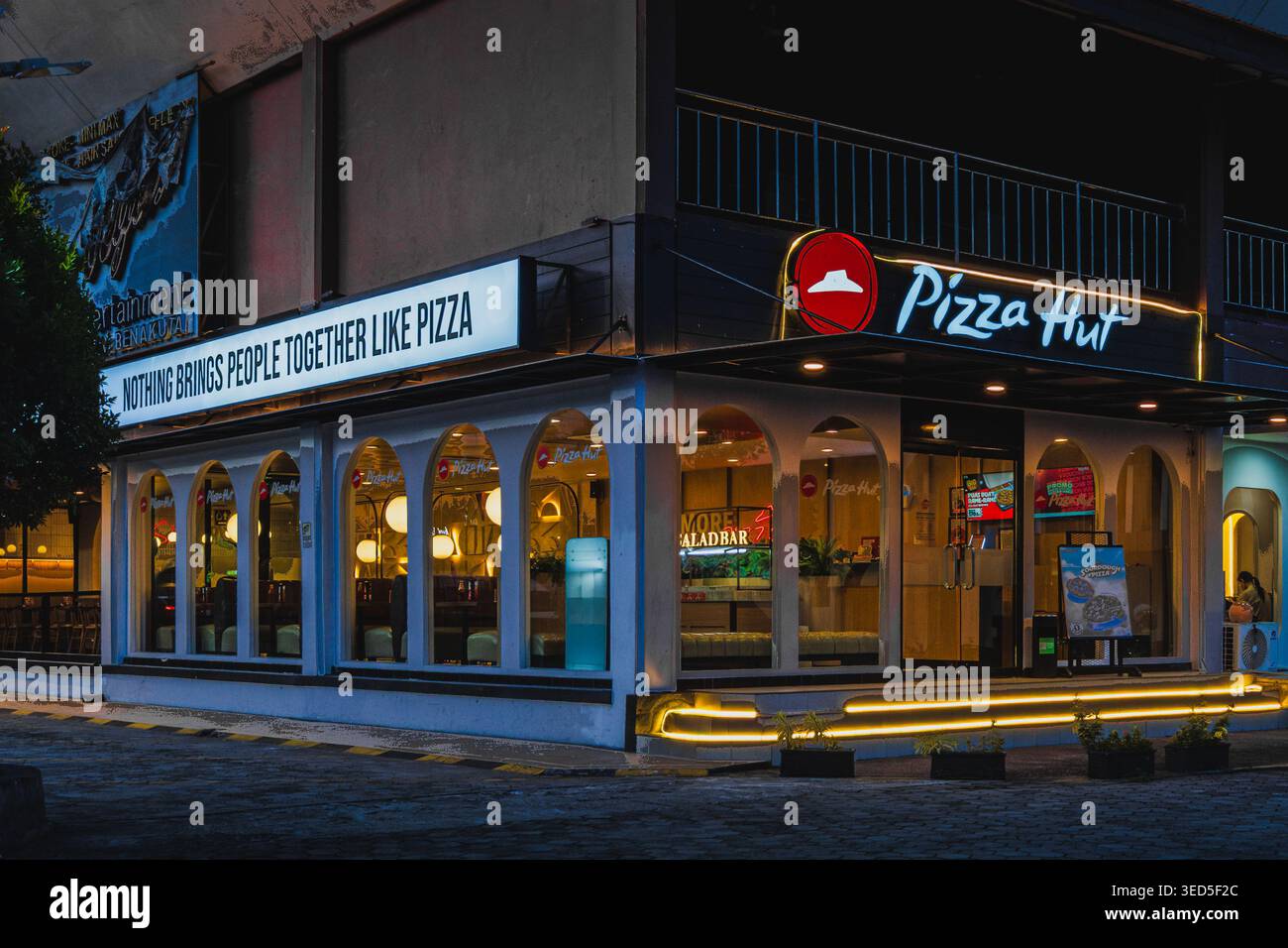 Balikpapan, Indonesia - aprile 29 2026. Un ristorante Pizza Hut catturato al crepuscolo con segnaletica illuminata, finestre ad arco e un cartello illuminato. Foto Stock