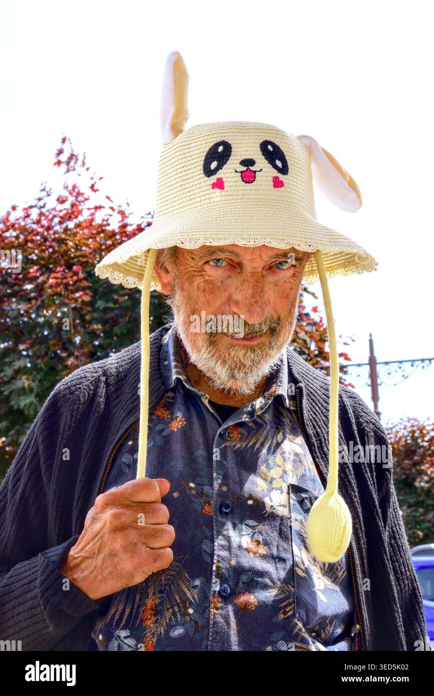 Vecchio che indossa un divertente cappello a maglia con orecchie a scomparsa pneumatiche - Preuilly-sur-Claise, Indre-et-Loire (37), Francia. Foto Stock