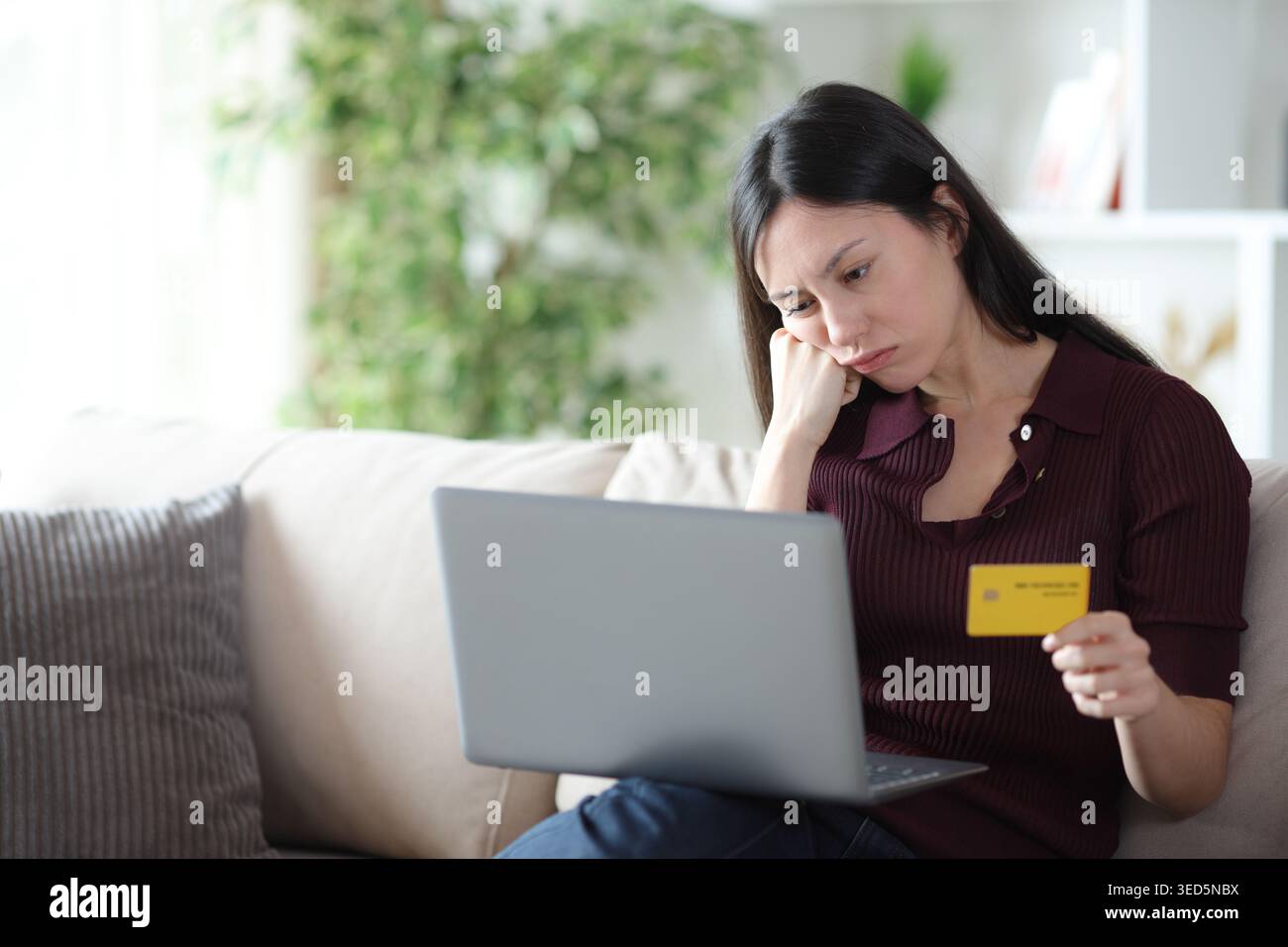 Annoiata donna asiatica che aspetta per molto tempo a pagare online con carta di credito e laptop a casa Foto Stock