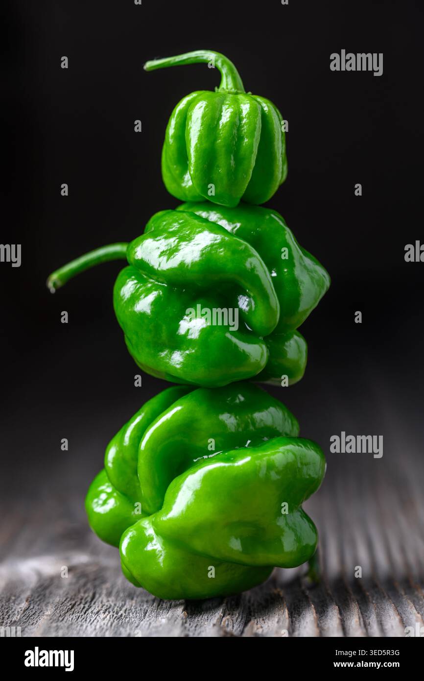 Pila di peperoni habanero verdi disposti verticalmente su una superficie di legno. Cialde di peperoncino fresco texture lucida composizione minimale Foto Stock