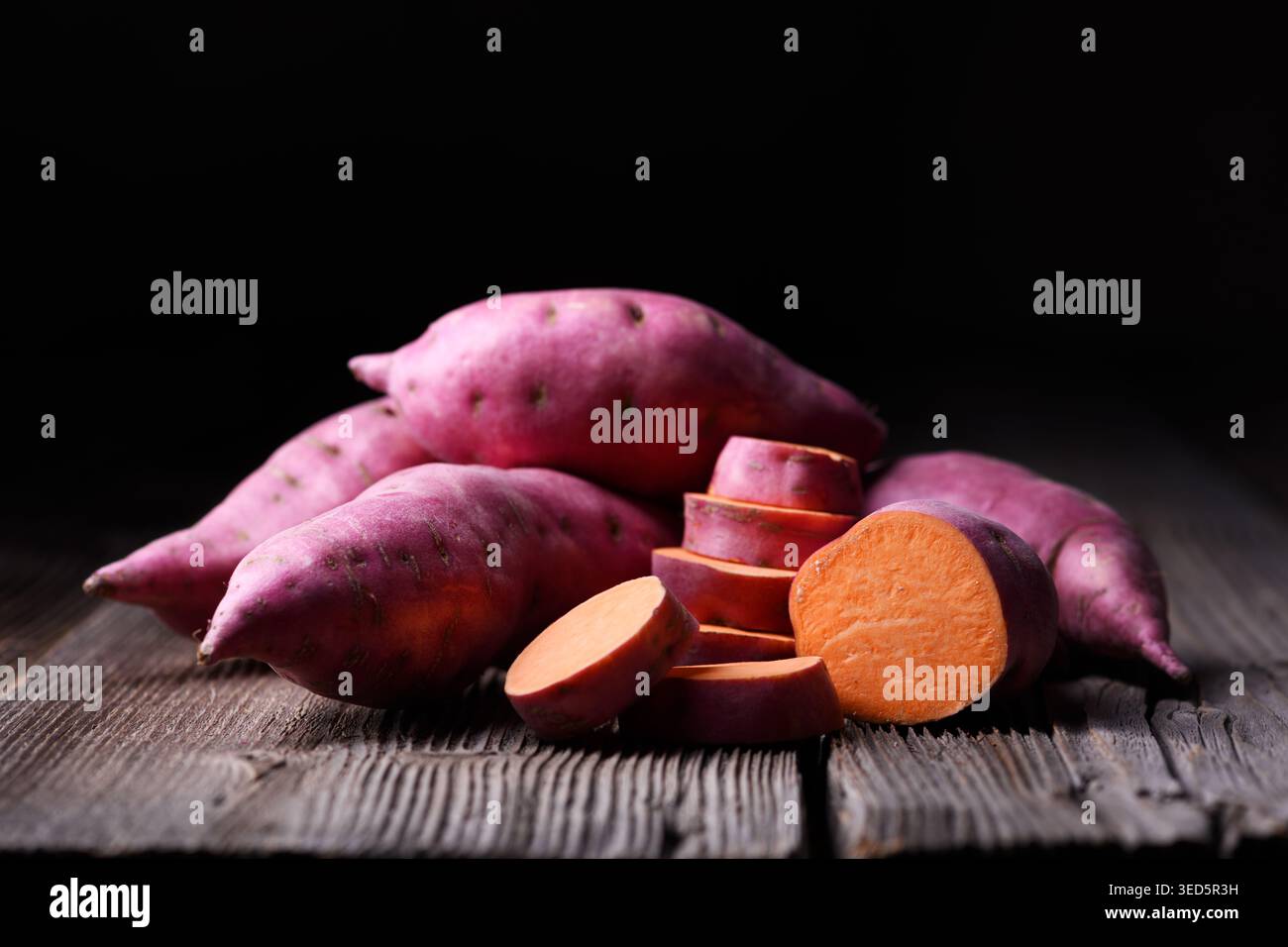 Patate dolci con pezzi tagliati su un tavolo di legno. Cibo vegetale biologico sano Foto Stock