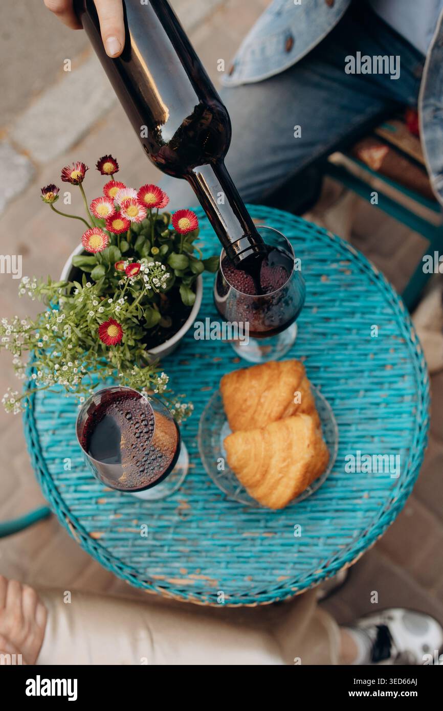 Versare vino rosso nei bicchieri durante la colazione all'aperto con croissant Foto Stock