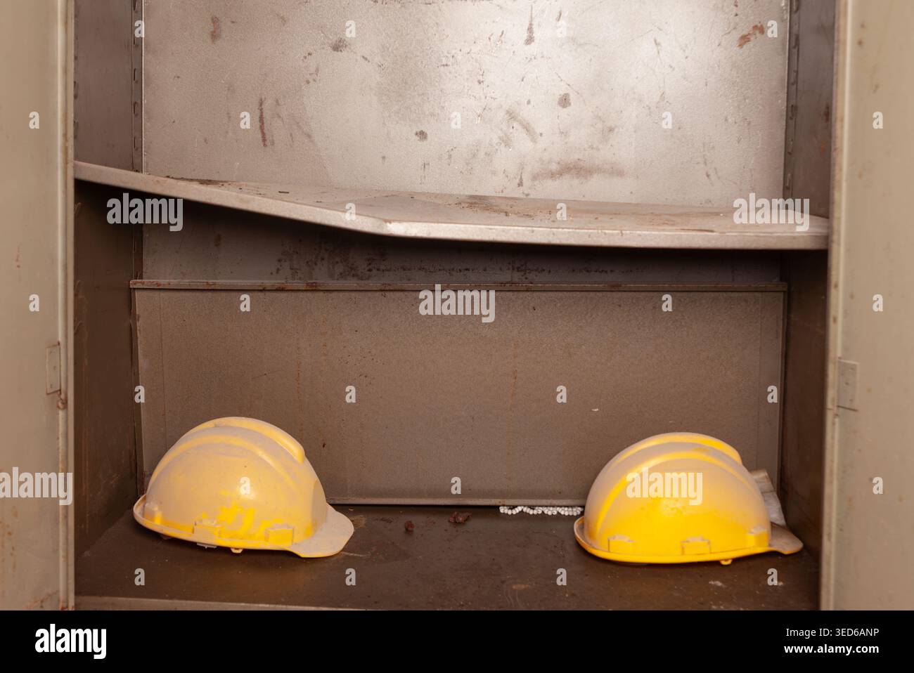 Due cappelli rigidi gialli con rivestimento di polvere poggiano fianco a fianco sul ripiano inferiore di un armadietto industriale in metallo. Foto Stock