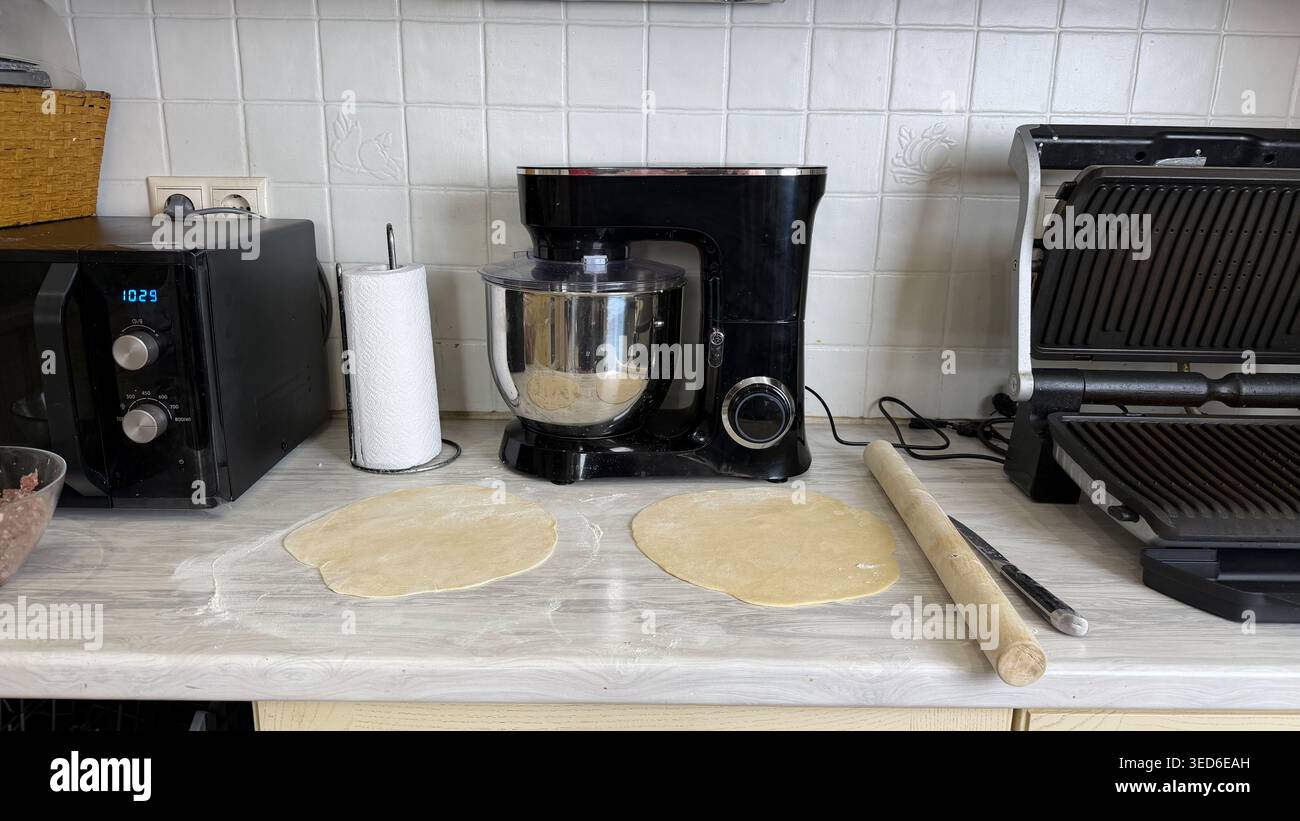 Impasto arrotolato sul ripiano della cucina con utensili da forno ed elettrodomestici nella moderna cucina domestica. Foto Stock